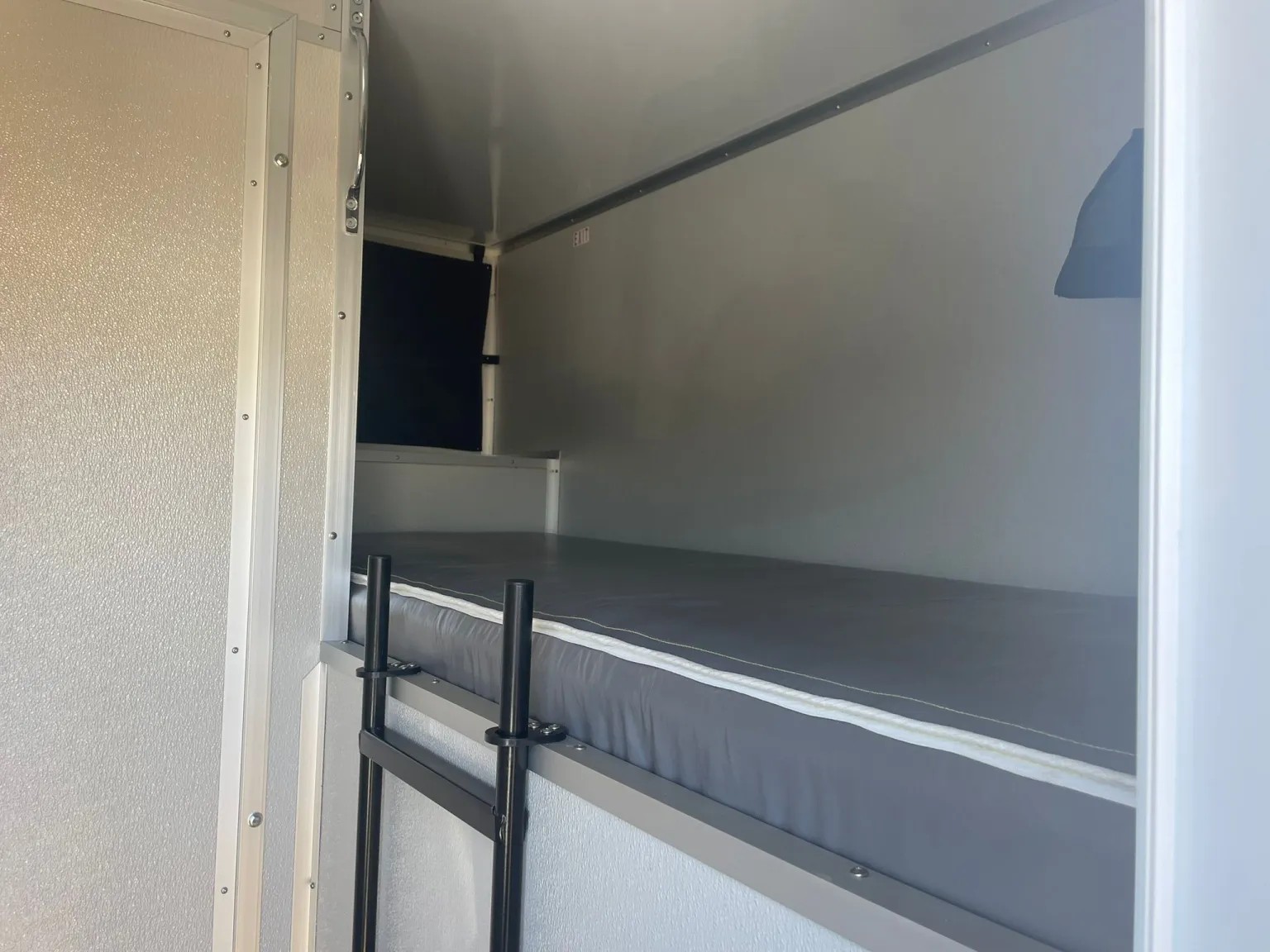 Padded bunk inside the sleeper trailer with a ladder to the upper bunk