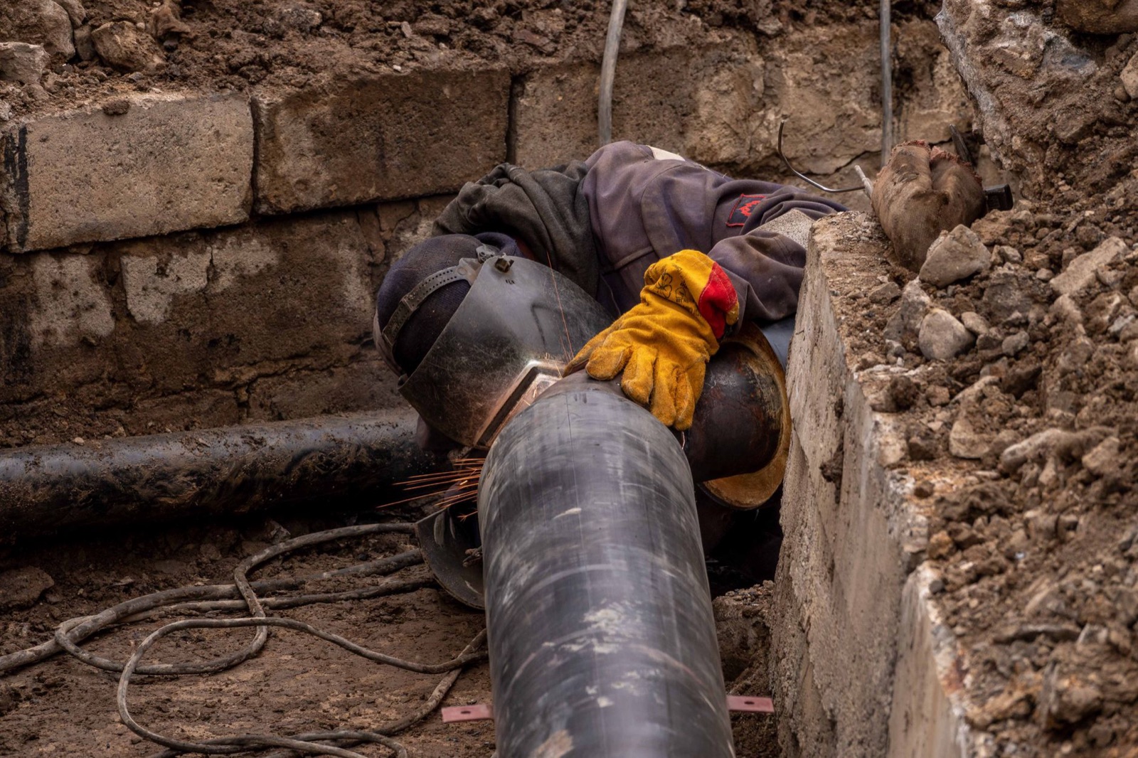 Welder in a trench joining coated steel pipe