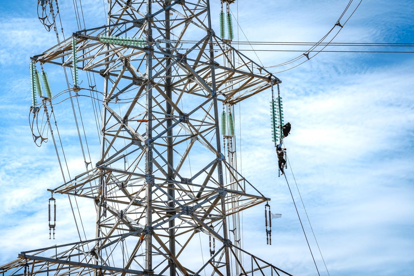 Linemen climbing a high-voltage transmission tower on a power line build